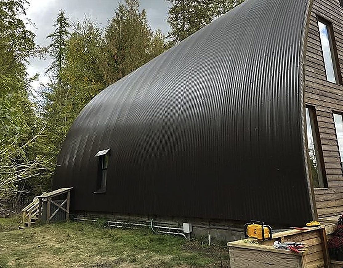 Large curved corrugated metal roof and wall system installed on an arched building in the North Idaho woods
