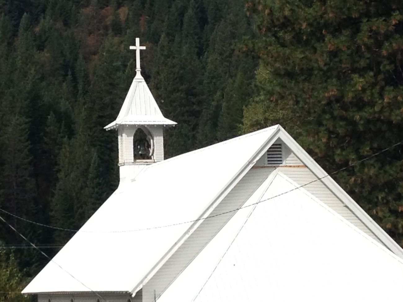 Church with a new Polar White metal roof and bell tower against a forested hillside
