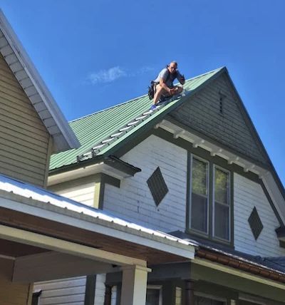 Roofer working on a green metal roof under a clear blue sky